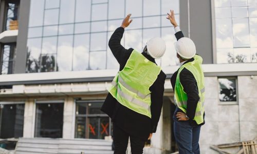constructores-multirraciales-pie-al-aire-libre-vista-posterior-vistiendo-uniforme-hablando-nuevo-edificio-cristal-trabajando-proyecto-infraestructura-ciudad_1157-50888