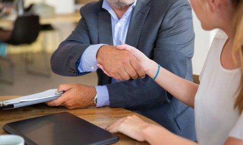 Mature legal advisor meeting with young customer at co-working, holding documents and shaking hands. Cropped shot. Paperwork or collaboration concept